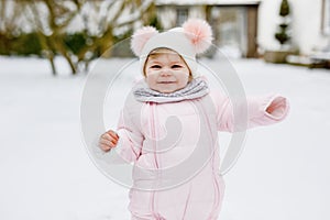 Happy little baby girl making first steps outdoors in winter through snow. Cute toddler learning walking. Child having