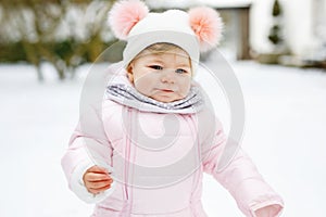 Happy little baby girl making first steps outdoors in winter through snow. Cute toddler learning walking. Child having