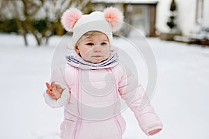 Happy little baby girl making first steps outdoors in winter through snow. Cute toddler learning walking. Child having