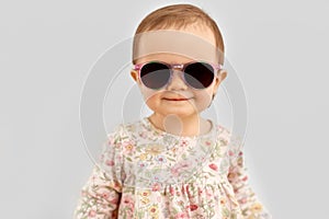 Happy little baby girl in sunglasses over grey