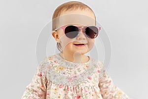 Happy little baby girl in sunglasses over grey