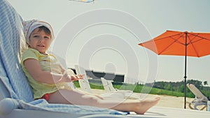 Happy little baby girl take sunbath in chair at beach