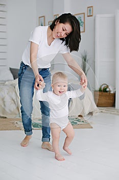 Happy little baby learning to walk with mother help in the bedroom