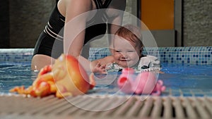 A happy little baby learns to swim in the pool with a caring mother.