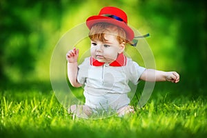 Happy little baby in red hat having fun in the park on solar glade. Summer vacations concept. The emotions.