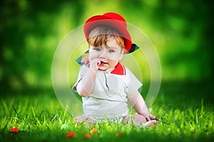 Happy little baby in red hat having fun in the park on solar glade. Summer vacations concept. The emotions.