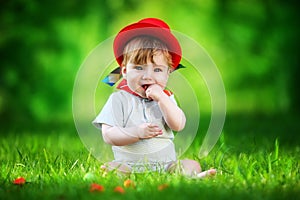 Happy little baby in red hat having fun in the park on solar glade. Summer vacations concept. The emotions.