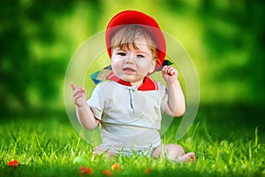 Happy little baby in red hat having fun in the park on solar glade. Summer vacations concept. The emotions.