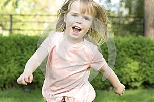 Happy little beautiful caucasoid girl runs in the park on the green grass