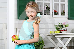 Happy little beautiful girl holds apple near white table