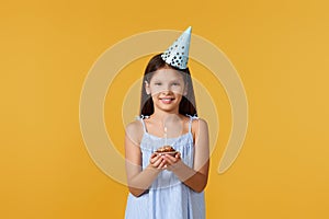 Happy little birthday girl with party cone holding cupcake