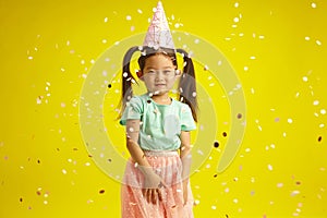 Happy Little Birthday Girl Surrounded Festive Confetti Celebrates fun Children's Holiday Against Bright Yellow