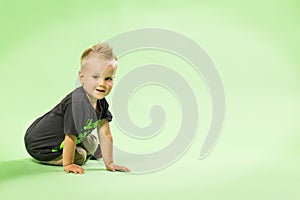 Happy little blond boy sitting green bacground