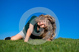 Happy little blond child laying on the grass in the park. Smmer day during school holidays. Amazed kid boy dreaming and