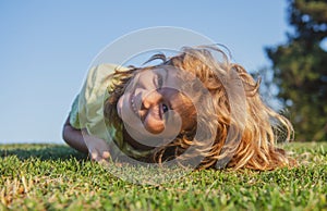 Happy little blond child laying on the grass in the park. Smmer day during school holidays. Amazed kid boy dreaming and