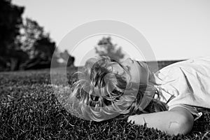 Happy little blond child laying on the grass in the park. Smmer day during school holidays. Amazed kid boy dreaming and