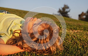 Happy little blond child laying on the grass in the park. Smmer day during school holidays. Kid boy dreaming and smiling