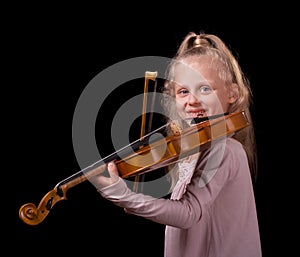 Happy little blond girl learns to play the violin isolated on black