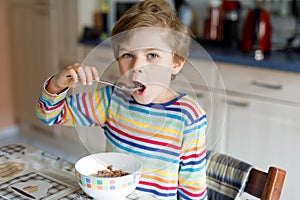 Happy little blond kid boy eating cereals for breakfast or lunch. Healthy eating for children.