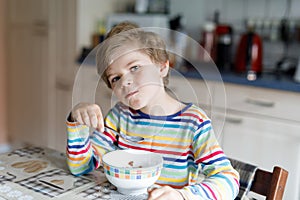 Happy little blond kid boy eating cereals for breakfast or lunch. Healthy eating for children.