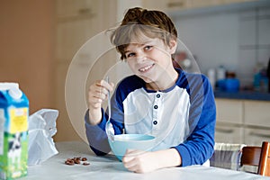 Happy little blond kid boy eating cereals for breakfast or lunch. Healthy eating for children. Child in colorful pajama