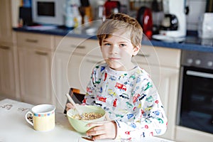 Happy little blond kid boy eating cereals for breakfast or lunch. Healthy eating for children in the morning. Child in