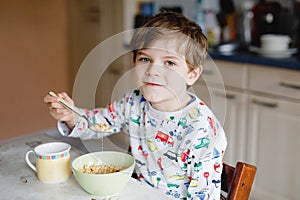 Happy little blond kid boy eating cereals for breakfast or lunch. Healthy eating for children in the morning. Child in