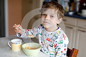 Happy little blond kid boy eating cereals for breakfast or lunch. Healthy eating for children in the morning. Child in