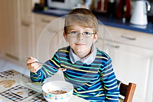 Happy little blond kid boy eating cereals for breakfast or lunch. Healthy eating for children.