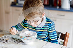 Happy little blond kid boy eating cereals for breakfast or lunch. Healthy eating for children.