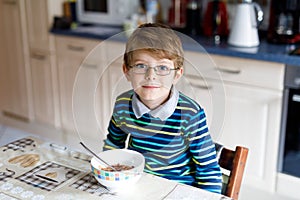 Happy little blond kid boy eating cereals for breakfast or lunch. Healthy eating for children.