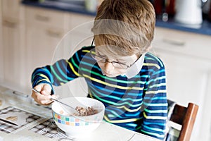 Happy little blond kid boy eating cereals for breakfast or lunch. Healthy eating for children.