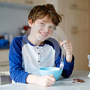 Happy little blond kid boy eating cereals for breakfast or lunch. Healthy eating for children. Child in colorful pajama