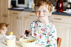 Happy little blond kid boy eating cereals for breakfast or lunch. Healthy eating for children in the morning. Child in