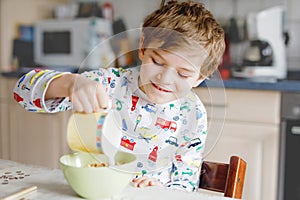 Happy little blond kid boy eating cereals for breakfast or lunch. Healthy eating for children in the morning. Child in