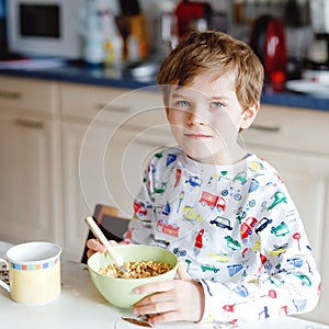 Happy little blond kid boy eating cereals for breakfast or lunch. Healthy eating for children in the morning. Child in