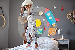 Happy little boy with astronaut helmet jumping on bed