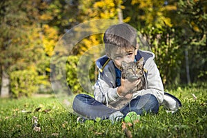 Happy little boy in the autumn park with pet kitten.