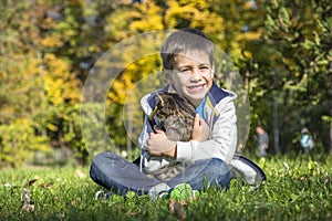 Happy little boy in the autumn park with pet kitten.