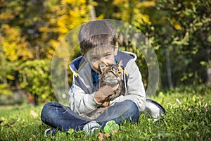 Happy little boy in the autumn park with pet kitten.