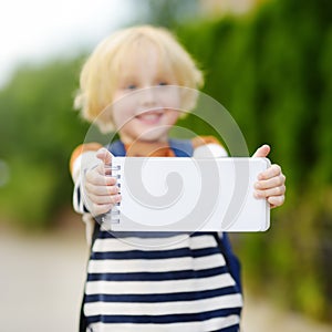 Happy little boy with backpack going to school. Child holding with hands empty white blank card for copy space and free text.