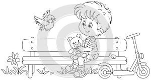 Happy little boy on a bench and a small bird in a summer park