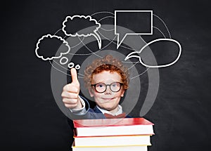 Happy little boy and blank speech clouds bubbles. Smart kid in glasses on school blackboard background