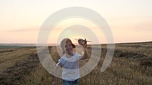 Happy little boy child in helmet aviator pilot of airplane running with toy wooden plane in field