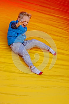 Happy little boy child rides on an inflatable multi-colored slide