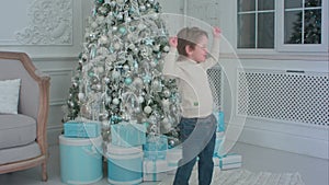Happy little boy dancing next to the Christmas tree and presents