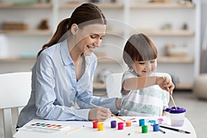 Happy little boy drawing picture with teacher at art school, developing creativity skills with paints, empty space