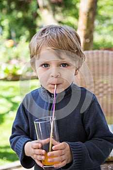 Happy little boy drinking orange juice with straw