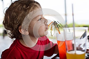 Happy little boy drinking orange juice with straw