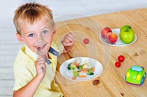 Happy little boy eating mixed vegetables salad on wooden table